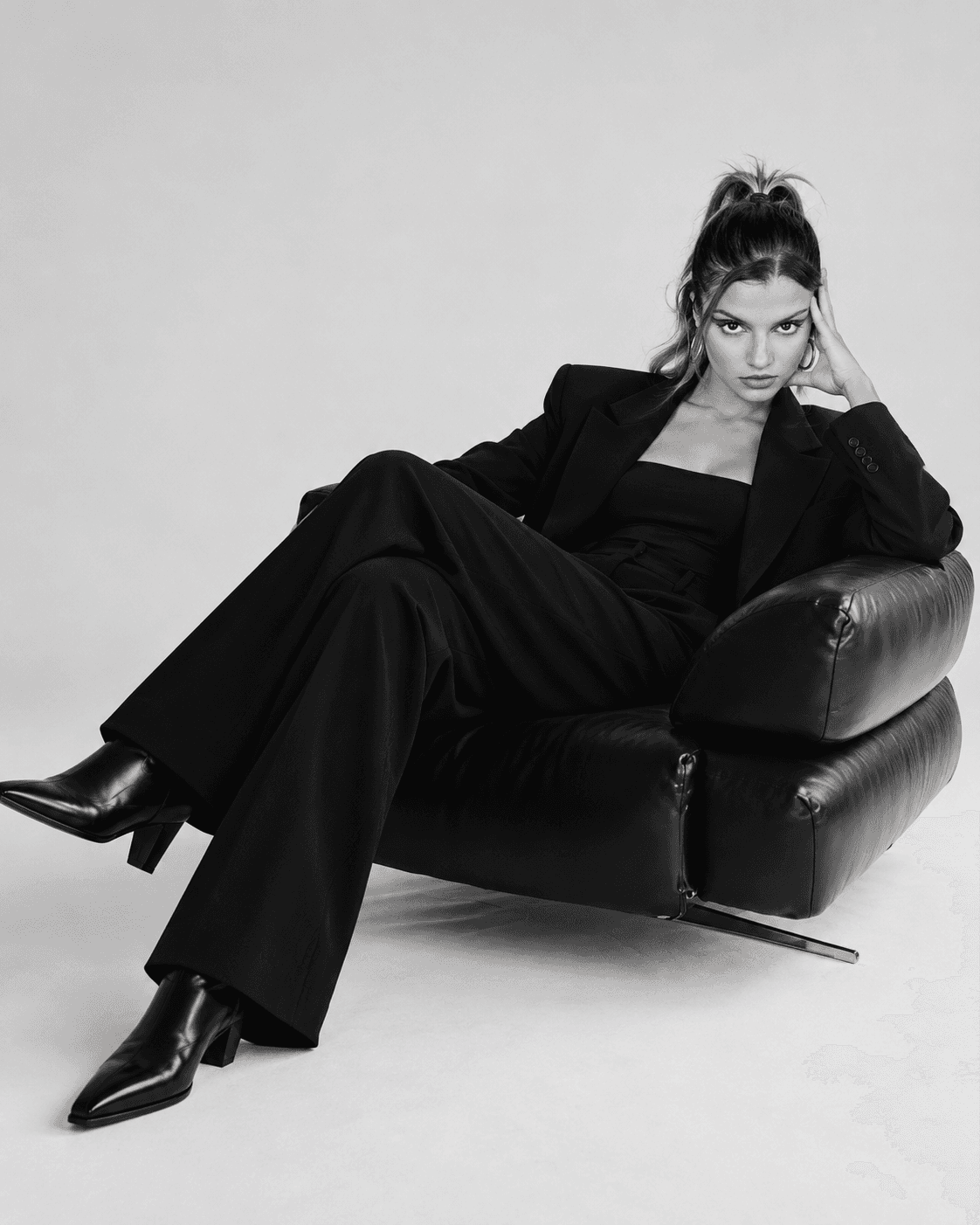Fatima Zahra El Amri in a black suit, lounging in a black leather chair